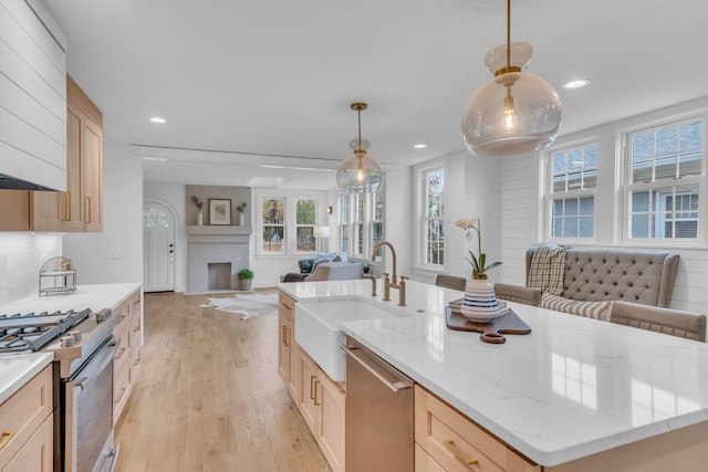 kitchen featuring pendant lighting, light brown cabinets, sink, an island with sink, and stainless steel appliances