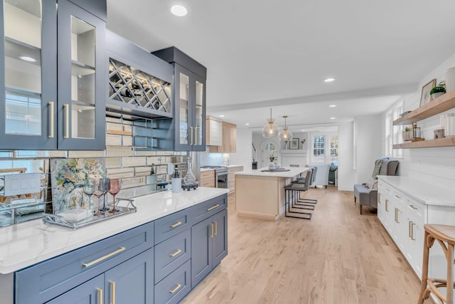 kitchen featuring hanging light fixtures, backsplash, an island with sink, a kitchen bar, and light wood-type flooring