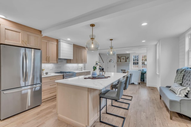 kitchen featuring light brown cabinetry, hanging light fixtures, appliances with stainless steel finishes, and an island with sink