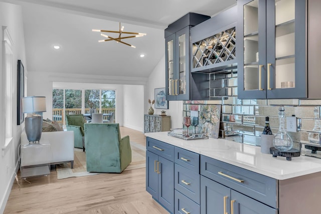 kitchen featuring light stone countertops, light wood-type flooring, backsplash, a chandelier, and lofted ceiling