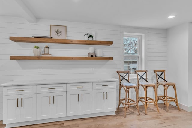 bar featuring light hardwood / wood-style floors, light stone counters, white cabinetry, and beam ceiling