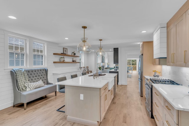 kitchen with sink, stainless steel appliances, decorative light fixtures, decorative backsplash, and light wood-type flooring