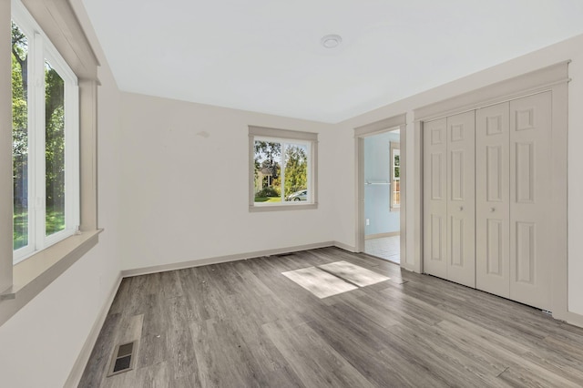 unfurnished bedroom with multiple windows, a closet, and light hardwood / wood-style flooring