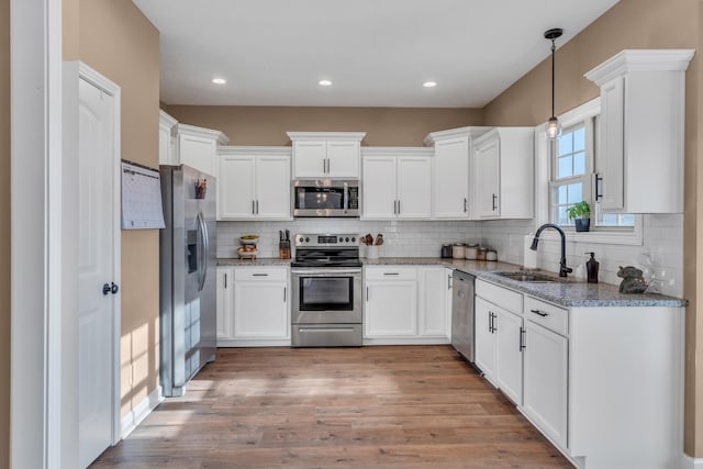 kitchen with light stone countertops, appliances with stainless steel finishes, sink, white cabinets, and hanging light fixtures