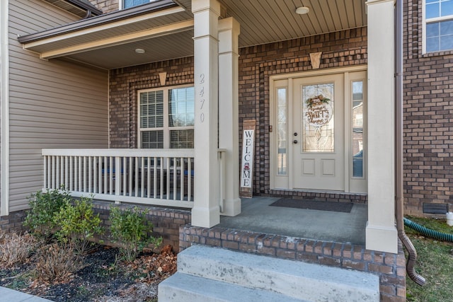 view of exterior entry with a porch and brick siding