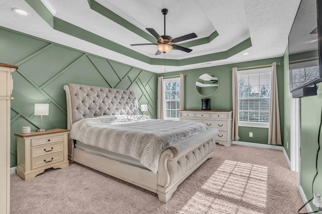 carpeted bedroom featuring a raised ceiling, multiple windows, ceiling fan, and crown molding