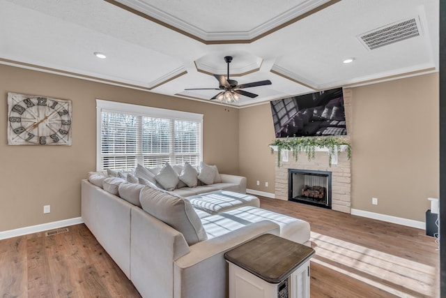 living room with ceiling fan, a stone fireplace, light wood-type flooring, and crown molding