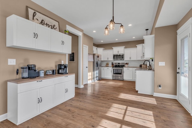 kitchen featuring white cabinetry, decorative light fixtures, decorative backsplash, appliances with stainless steel finishes, and light wood-type flooring