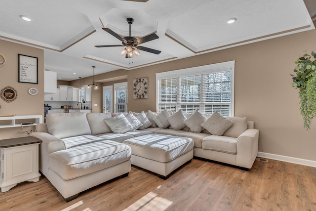 living room with ceiling fan, light wood-type flooring, ornamental molding, and coffered ceiling