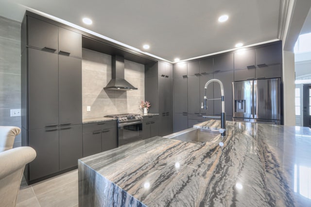 kitchen with sink, dark stone countertops, light tile patterned floors, stainless steel appliances, and wall chimney exhaust hood