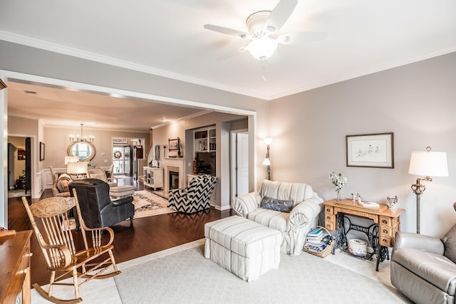 living room featuring a fireplace, wood-type flooring, ceiling fan with notable chandelier, and crown molding