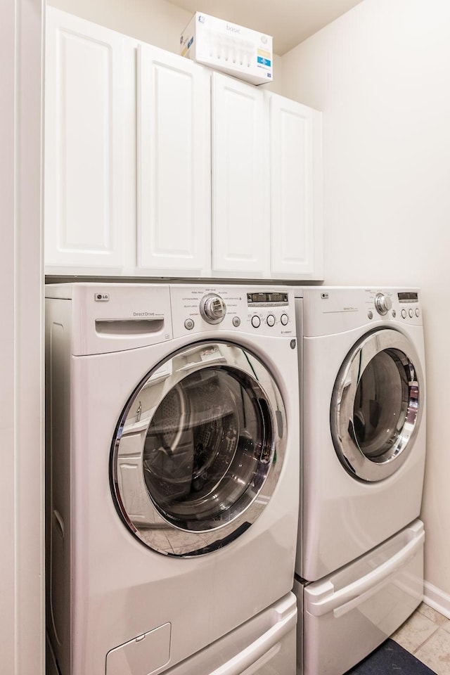 clothes washing area featuring washer and clothes dryer, light tile patterned flooring, and cabinets