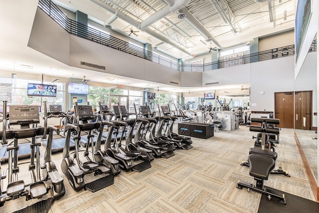 workout area with ceiling fan, light colored carpet, and a towering ceiling