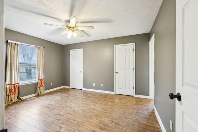 unfurnished bedroom with two closets, ceiling fan, a textured ceiling, and light wood-type flooring