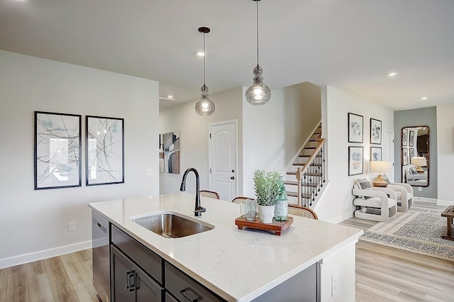 kitchen featuring a kitchen island with sink, hanging light fixtures, sink, stainless steel dishwasher, and light stone counters