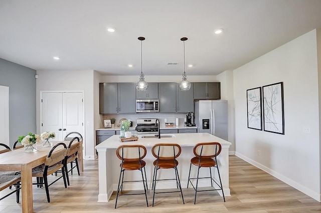 kitchen featuring gray cabinetry, stainless steel appliances, a kitchen island with sink, sink, and light hardwood / wood-style floors