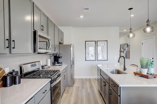 kitchen featuring sink, appliances with stainless steel finishes, tasteful backsplash, decorative light fixtures, and light stone counters