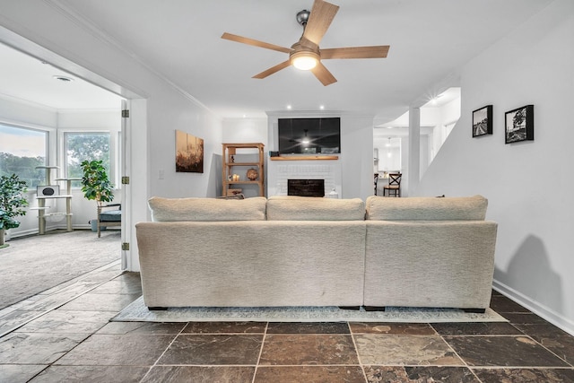 living room with ceiling fan, dark carpet, crown molding, and a fireplace