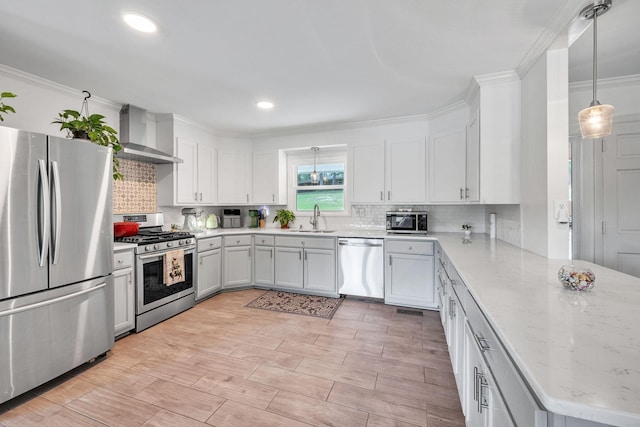 kitchen with sink, wall chimney range hood, decorative light fixtures, white cabinets, and appliances with stainless steel finishes