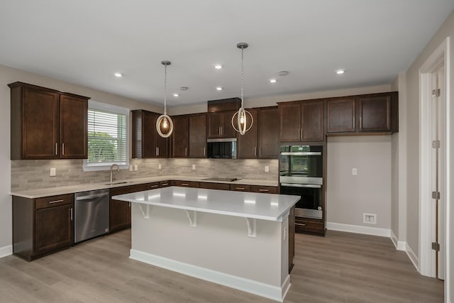 kitchen with a center island, sink, hanging light fixtures, appliances with stainless steel finishes, and light hardwood / wood-style floors