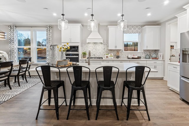 kitchen featuring white cabinets, decorative light fixtures, stainless steel appliances, and light hardwood / wood-style flooring