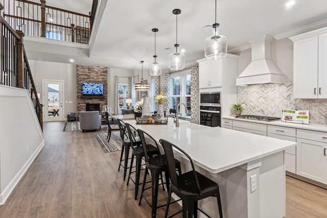 kitchen with pendant lighting, custom exhaust hood, a spacious island, a fireplace, and black oven