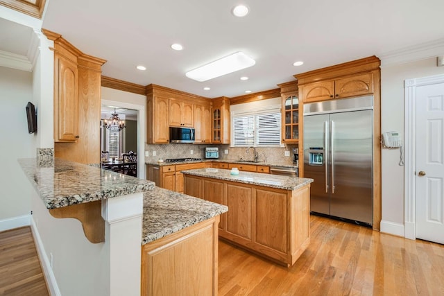 kitchen featuring stainless steel appliances, kitchen peninsula, light stone counters, a kitchen island, and sink