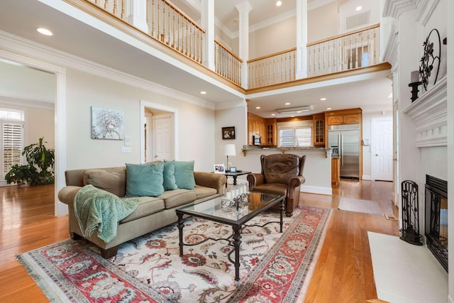 living room featuring a high ceiling, a healthy amount of sunlight, ornamental molding, and light wood-type flooring