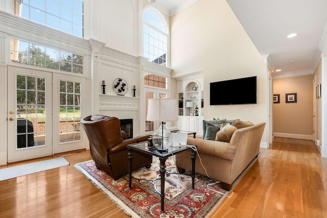 living room featuring a high ceiling, light wood-type flooring, built in shelves, and ornamental molding