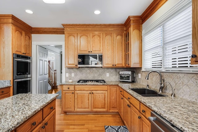 kitchen featuring appliances with stainless steel finishes, light stone counters, sink, light hardwood / wood-style flooring, and tasteful backsplash