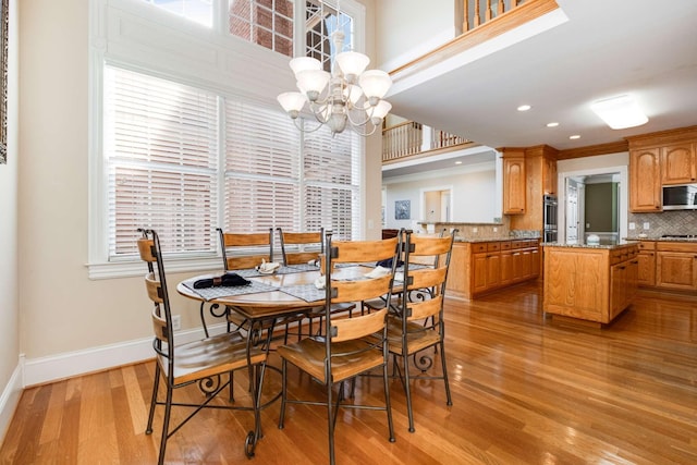 dining space featuring a towering ceiling, an inviting chandelier, and light hardwood / wood-style floors