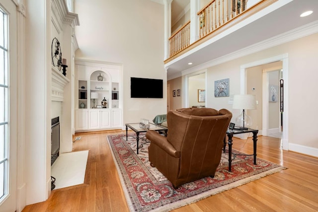 living room featuring a towering ceiling, ornamental molding, built in shelves, and light hardwood / wood-style flooring