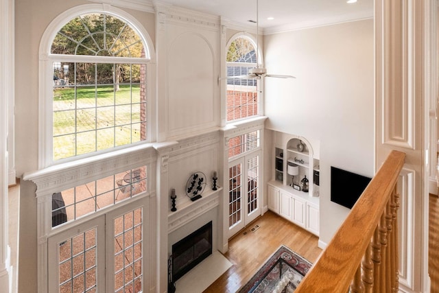 interior space featuring a towering ceiling, light hardwood / wood-style flooring, ornamental molding, ceiling fan, and built in shelves