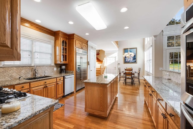 kitchen featuring light stone counters, a wealth of natural light, a kitchen island, appliances with stainless steel finishes, and sink