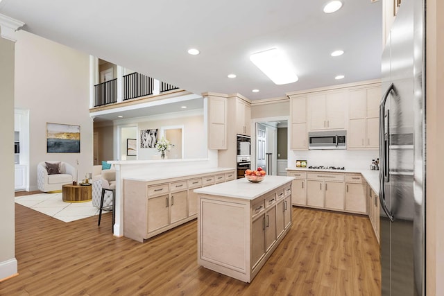 kitchen featuring appliances with stainless steel finishes, crown molding, kitchen peninsula, a kitchen island, and light hardwood / wood-style flooring