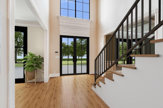 foyer entrance featuring french doors, a high ceiling, crown molding, and light hardwood / wood-style flooring