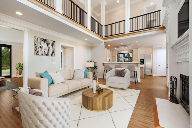 living room with a high ceiling, a tile fireplace, light hardwood / wood-style floors, and crown molding