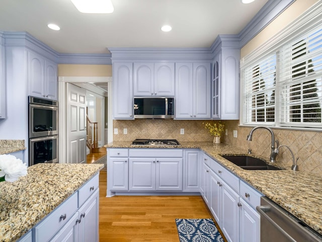 kitchen with light stone counters, sink, light wood-type flooring, and appliances with stainless steel finishes