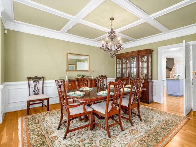 dining area with ornamental molding, coffered ceiling, a chandelier, and light wood-type flooring