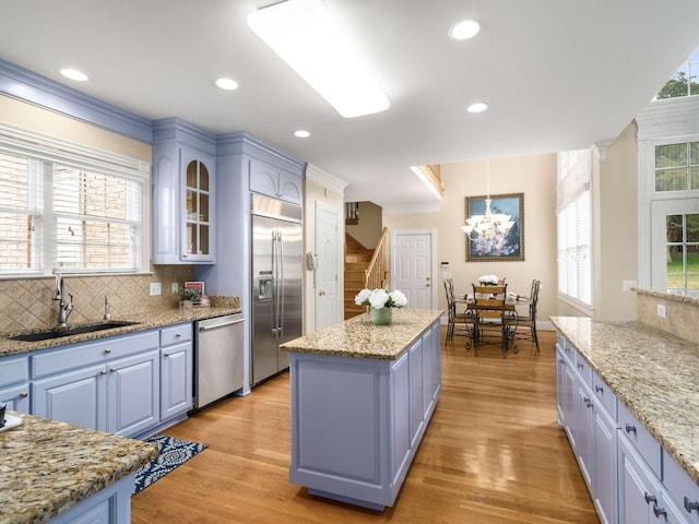 kitchen with appliances with stainless steel finishes, light stone countertops, a kitchen island, and light wood-type flooring