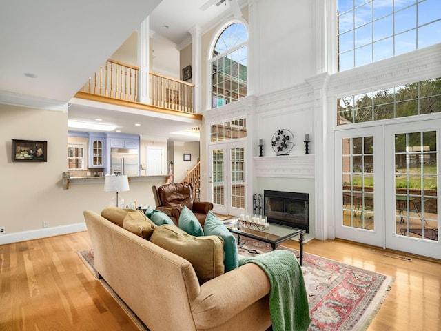 living room with a towering ceiling, a fireplace, ornamental molding, light hardwood / wood-style floors, and french doors