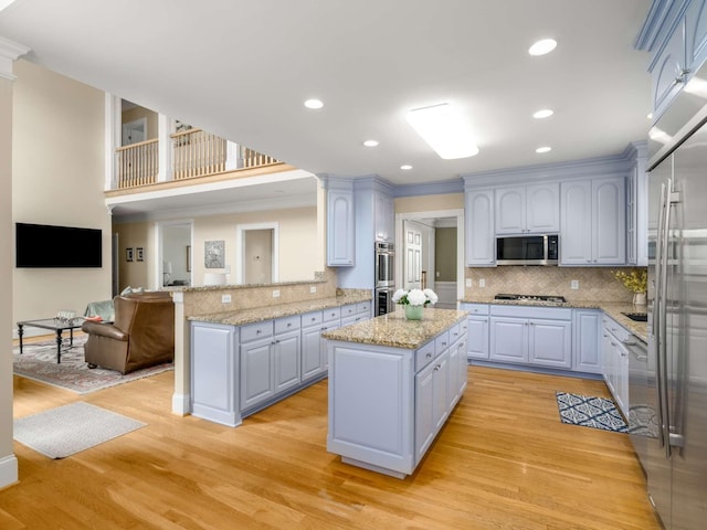 kitchen featuring light hardwood / wood-style flooring, backsplash, stainless steel appliances, a kitchen island, and kitchen peninsula