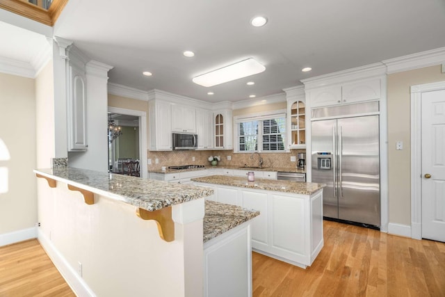 kitchen with glass insert cabinets, a peninsula, light wood-type flooring, appliances with stainless steel finishes, and a sink