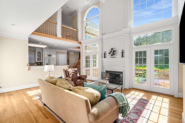 living room featuring a towering ceiling, baseboards, ornamental molding, a fireplace, and wood finished floors