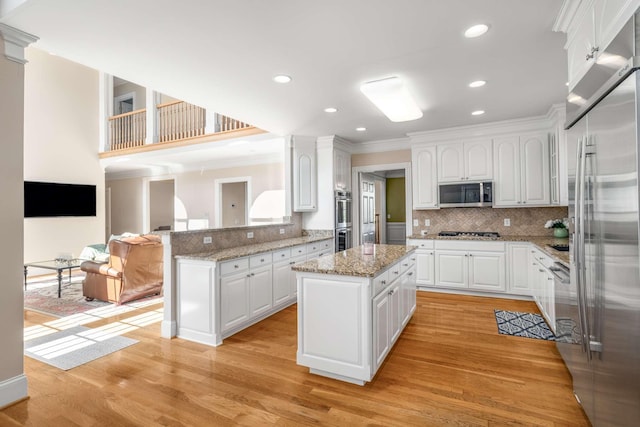 kitchen featuring a center island, appliances with stainless steel finishes, a peninsula, light wood finished floors, and decorative backsplash