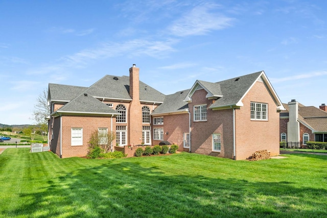 rear view of property with a yard, a chimney, fence, brick siding, and roof with shingles