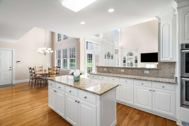 kitchen featuring light wood-style floors, white cabinets, a center island, a notable chandelier, and backsplash