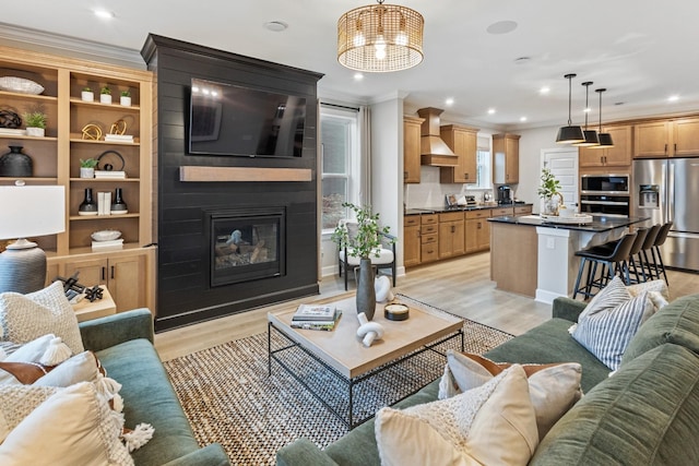 living room featuring a large fireplace, crown molding, and light hardwood / wood-style flooring