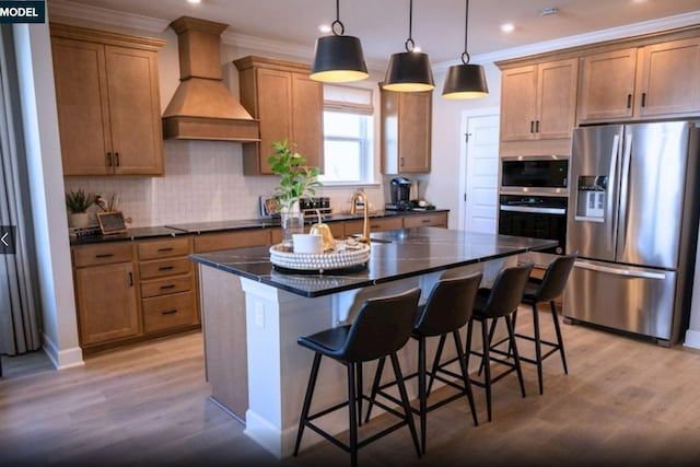 kitchen with appliances with stainless steel finishes, light wood-type flooring, an island with sink, and custom exhaust hood