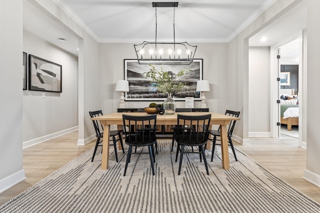 dining area with light wood-type flooring, crown molding, and a notable chandelier